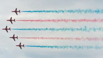 Five British Royal Air Forces jets fly in formation dispensing smokes of various colors.