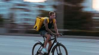 Tattooed man on bicycle with a large backpack for delivery food.